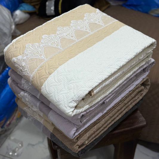 Stack of folded bedspreads with lace trim on a wooden surface